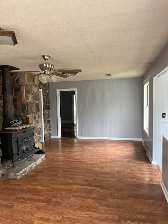 unfurnished living room with ceiling fan, dark hardwood / wood-style flooring, a wood stove, and a textured ceiling