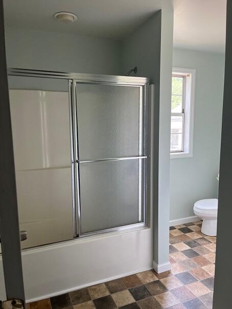 bathroom featuring combined bath / shower with glass door and toilet