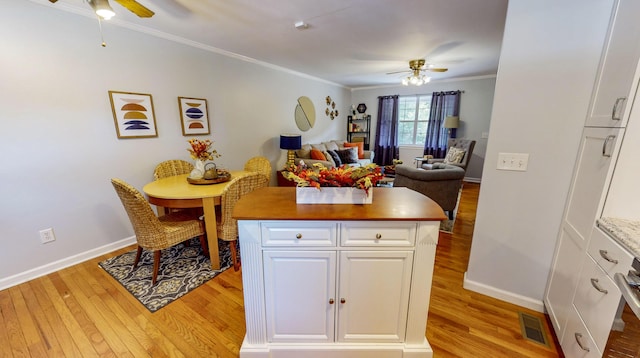 kitchen with ceiling fan, ornamental molding, white cabinets, and a kitchen island