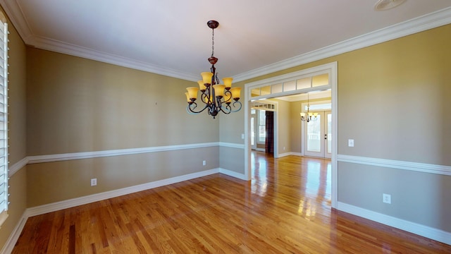 empty room with hardwood / wood-style floors, a notable chandelier, and ornamental molding