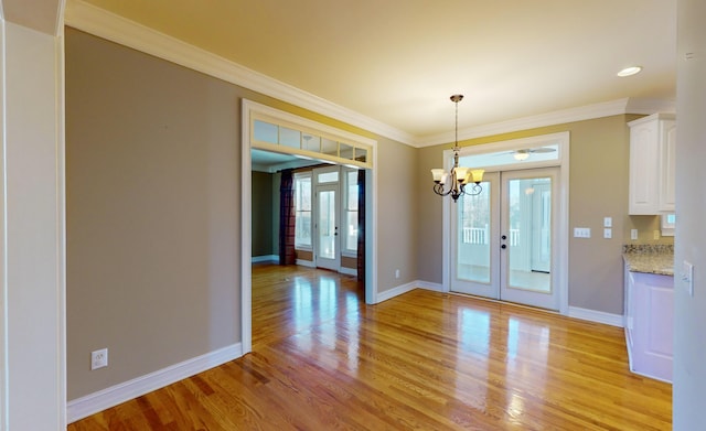 unfurnished dining area with a chandelier, french doors, light hardwood / wood-style floors, and ornamental molding