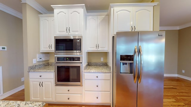 kitchen with white cabinetry, light stone countertops, stainless steel appliances, and ornamental molding