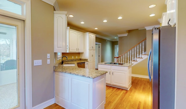 kitchen with sink, kitchen peninsula, light hardwood / wood-style floors, white cabinets, and appliances with stainless steel finishes