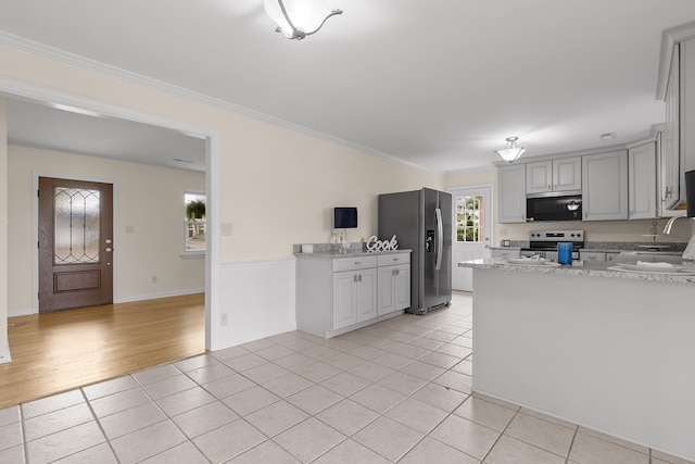 kitchen with light stone countertops, appliances with stainless steel finishes, kitchen peninsula, ornamental molding, and light hardwood / wood-style floors