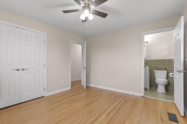 unfurnished bedroom with ensuite bathroom, ceiling fan, light wood-type flooring, tile walls, and a closet