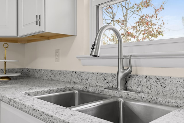 interior details featuring light stone countertops, sink, and white cabinets