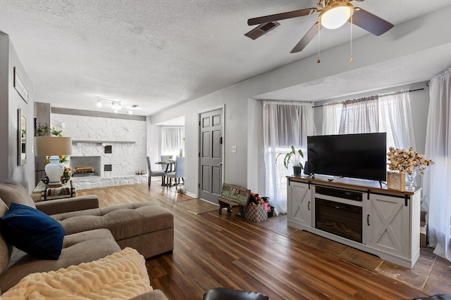 living room featuring wood-type flooring, a stone fireplace, ceiling fan, and a textured ceiling