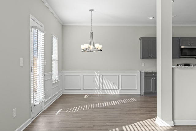 unfurnished dining area with wood-type flooring, ornamental molding, and an inviting chandelier