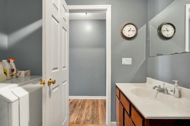 bathroom with a textured ceiling, wood finished floors, vanity, baseboards, and washer / dryer