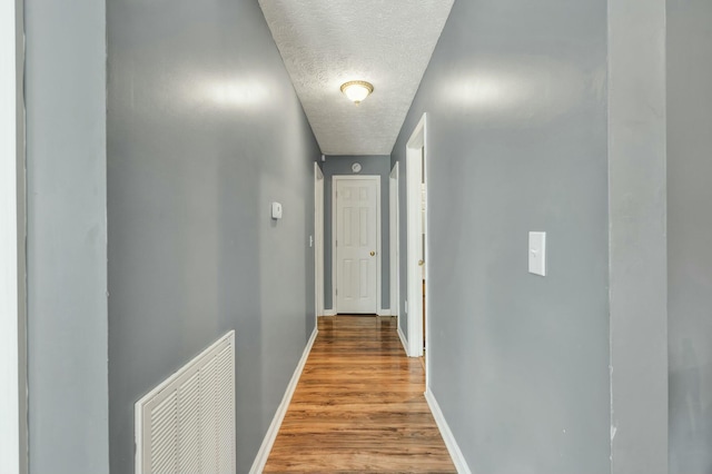 hallway with a textured ceiling, wood finished floors, visible vents, and baseboards