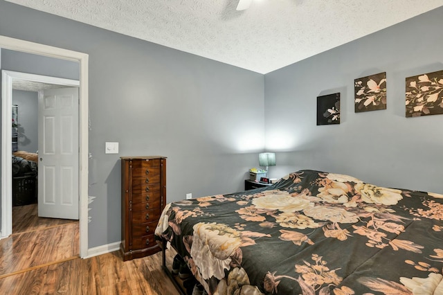 bedroom featuring a ceiling fan, a textured ceiling, baseboards, and wood finished floors