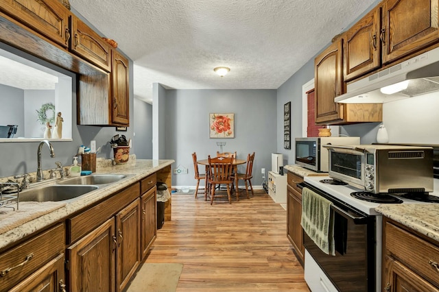 kitchen with under cabinet range hood, a sink, electric stove, light countertops, and light wood finished floors