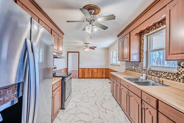 kitchen with under cabinet range hood, a wainscoted wall, stainless steel appliances, a sink, and marble finish floor