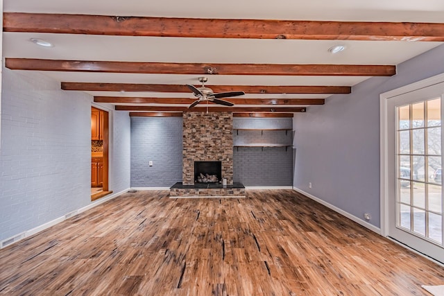 unfurnished living room with baseboards, a ceiling fan, brick wall, wood finished floors, and a stone fireplace