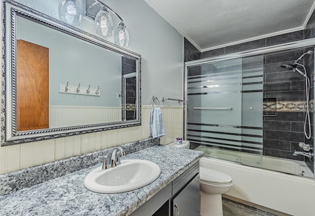 bathroom featuring toilet, a wainscoted wall, combined bath / shower with glass door, and crown molding