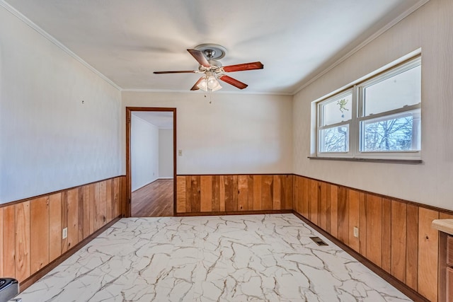 empty room with marble finish floor, crown molding, visible vents, wainscoting, and wood walls