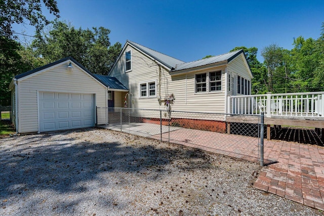 exterior space featuring fence, metal roof, a garage, a wooden deck, and gravel driveway