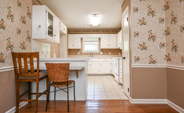 kitchen with white cabinetry, sink, a breakfast bar area, kitchen peninsula, and light wood-type flooring