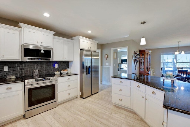 kitchen featuring light hardwood / wood-style floors, stainless steel appliances, decorative light fixtures, dark stone countertops, and white cabinets