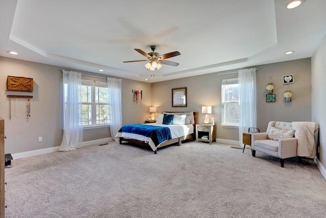 carpeted bedroom with ceiling fan, a tray ceiling, and multiple windows