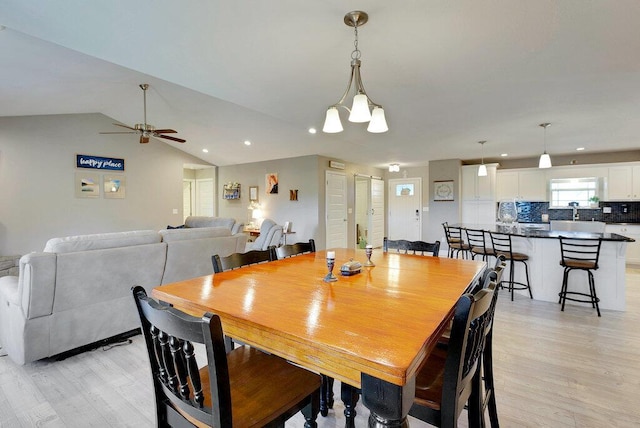 dining area with ceiling fan with notable chandelier, light hardwood / wood-style floors, and lofted ceiling