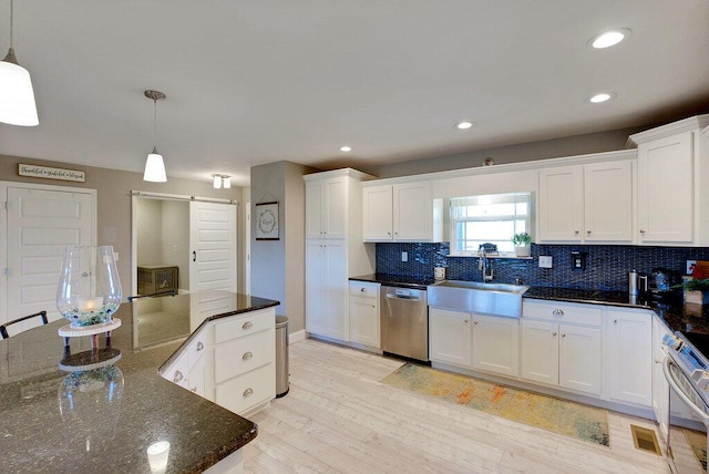 kitchen featuring a barn door, sink, hanging light fixtures, appliances with stainless steel finishes, and white cabinets