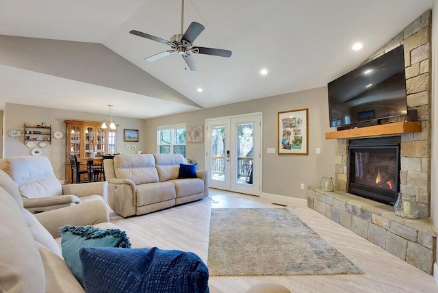 living room with light hardwood / wood-style floors, a stone fireplace, ceiling fan, lofted ceiling, and french doors