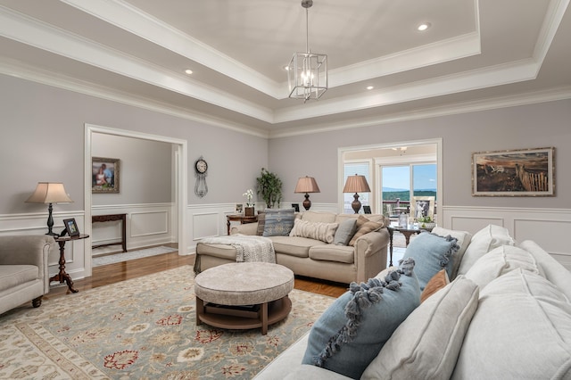 living room with a raised ceiling, crown molding, an inviting chandelier, and hardwood / wood-style flooring