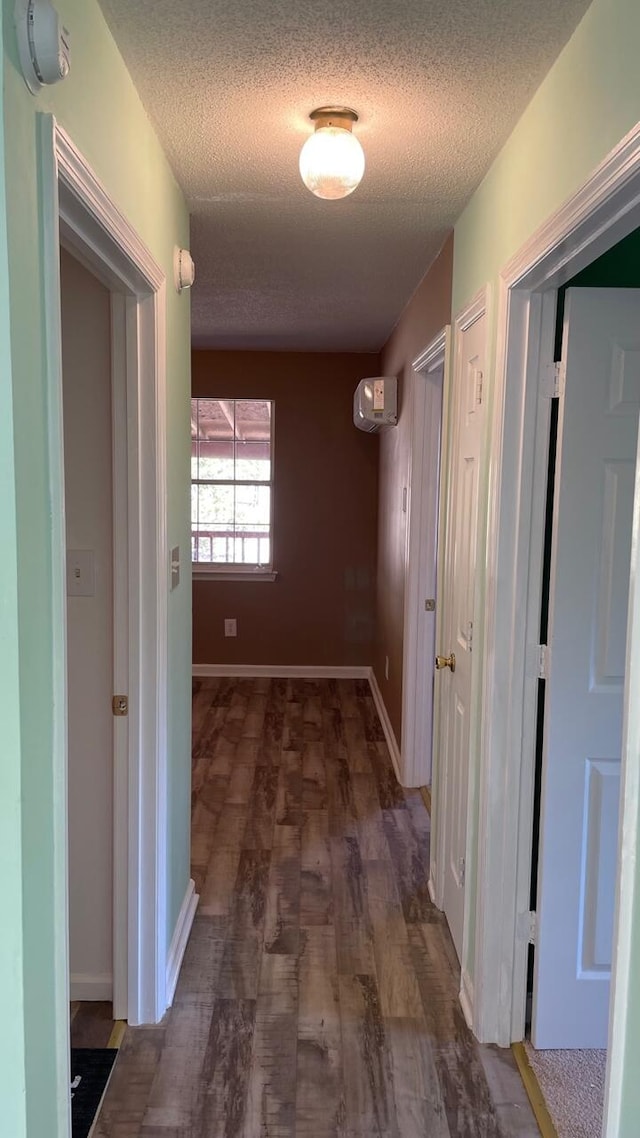 corridor featuring a wall unit AC, dark hardwood / wood-style flooring, and a textured ceiling