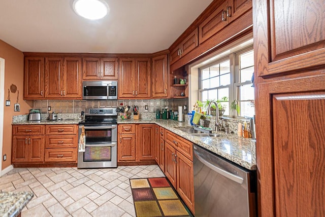 kitchen with tasteful backsplash, light stone counters, appliances with stainless steel finishes, brown cabinets, and a sink