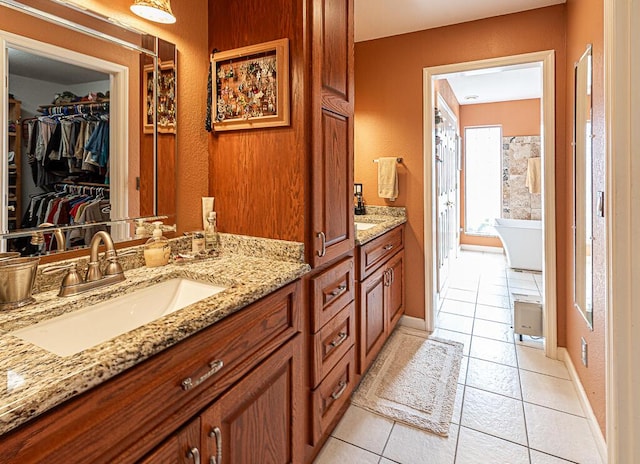 bathroom featuring a walk in closet, vanity, tile patterned flooring, a freestanding tub, and baseboards