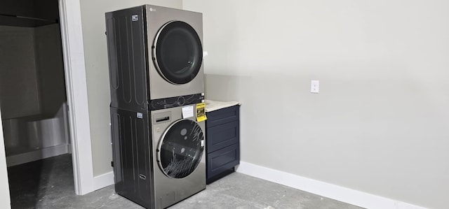 clothes washing area with stacked washer / drying machine and baseboards