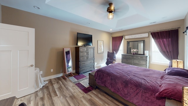 bedroom with ceiling fan, a raised ceiling, and light wood-type flooring