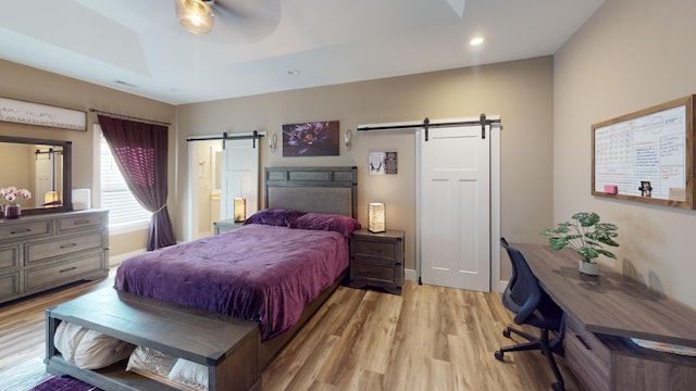 bedroom with connected bathroom, a tray ceiling, ceiling fan, a barn door, and light hardwood / wood-style floors