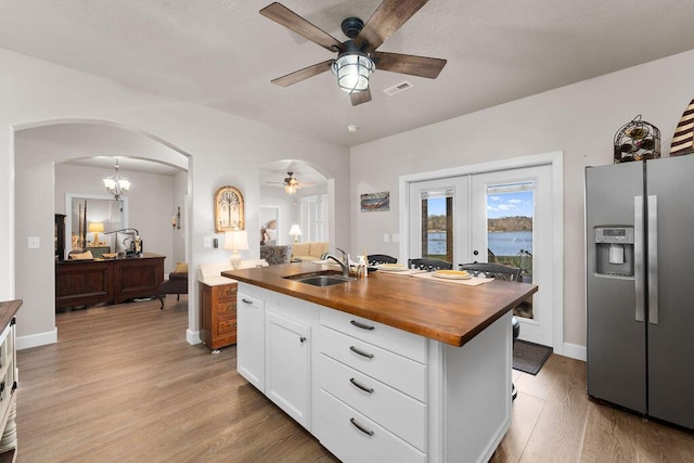 kitchen featuring sink, butcher block countertops, white cabinetry, a center island with sink, and stainless steel fridge