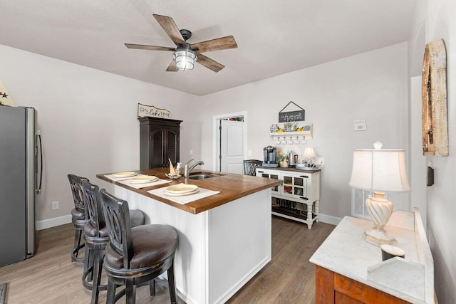 kitchen with butcher block countertops, stainless steel refrigerator, sink, dark hardwood / wood-style flooring, and a center island with sink