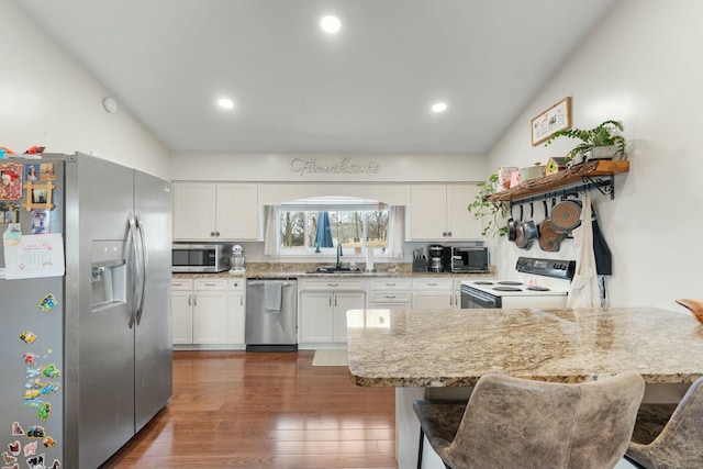 kitchen with light stone counters, dark hardwood / wood-style floors, a breakfast bar, white cabinets, and appliances with stainless steel finishes