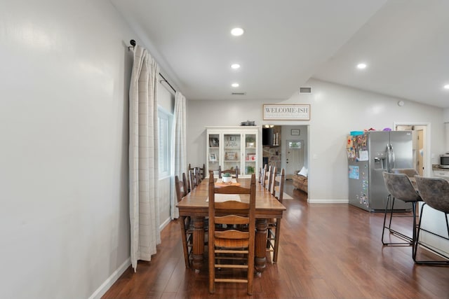 dining room with vaulted ceiling, a stone fireplace, and dark hardwood / wood-style floors