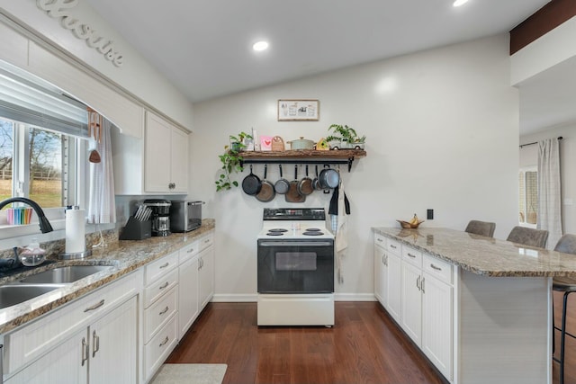 kitchen with a breakfast bar, white cabinets, electric stove, sink, and kitchen peninsula