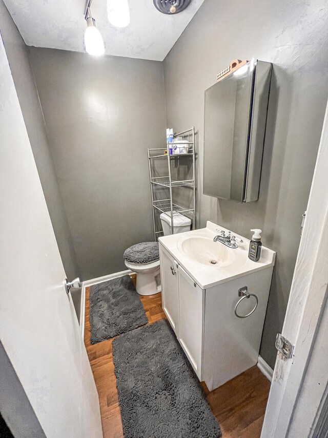 half bath with vanity, wood finished floors, toilet, and baseboards