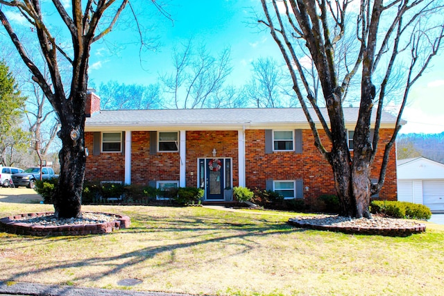 bi-level home with a chimney, a front lawn, a detached garage, and brick siding