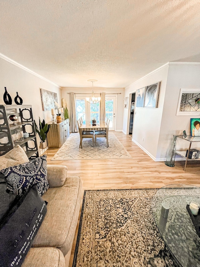 living room featuring a textured ceiling, crown molding, wood finished floors, baseboards, and an inviting chandelier