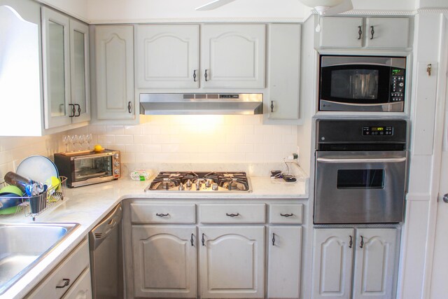 kitchen with tasteful backsplash, a toaster, stainless steel appliances, light countertops, and under cabinet range hood