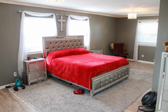 bedroom with a notable chandelier, baseboards, wood finished floors, and ornamental molding