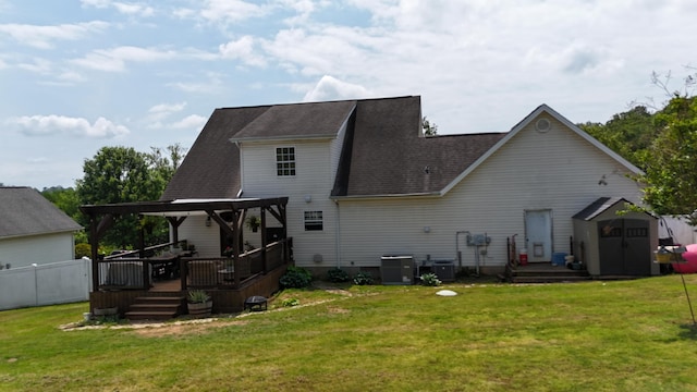 back of house with a deck, roof with shingles, a storage unit, a lawn, and an outbuilding