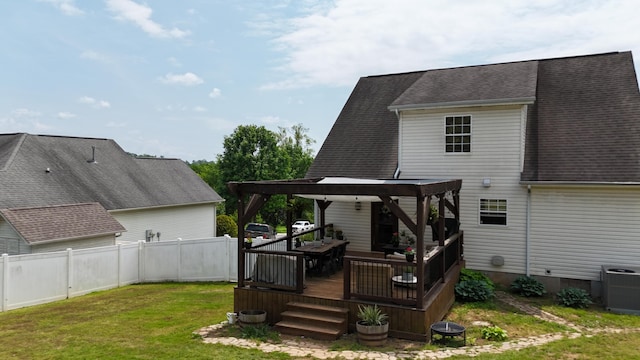 rear view of property featuring fence, a shingled roof, a wooden deck, central AC unit, and a yard