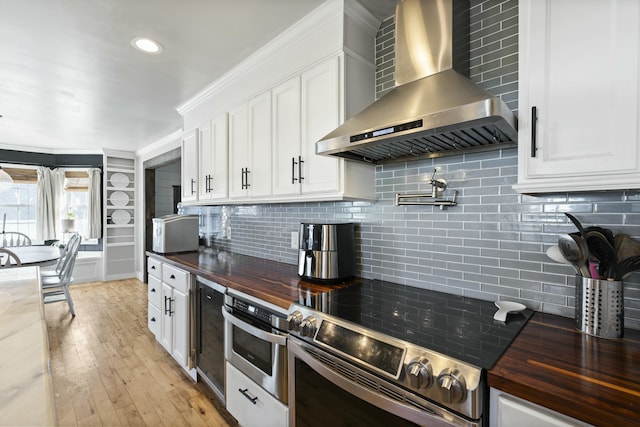 kitchen with butcher block counters, white cabinets, wall chimney range hood, and stainless steel appliances