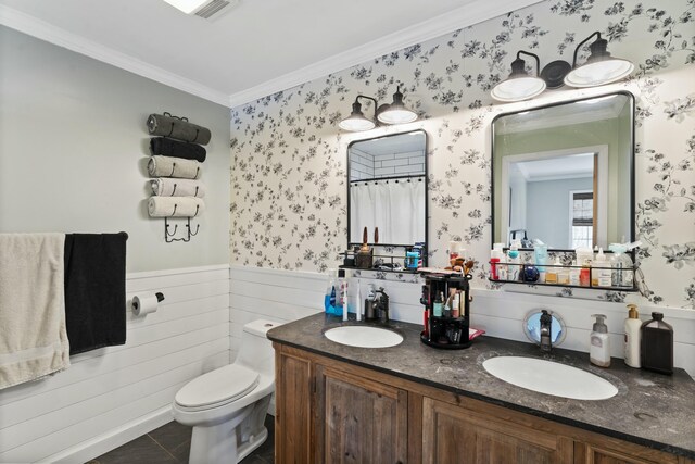 bathroom featuring ornamental molding, toilet, wallpapered walls, a wainscoted wall, and a sink
