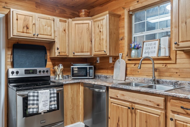 kitchen featuring light brown cabinetry, wooden walls, sink, and appliances with stainless steel finishes