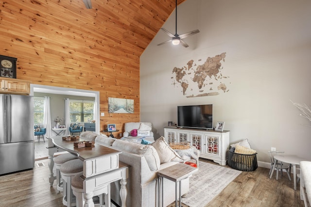 living room with wooden walls, hardwood / wood-style flooring, ceiling fan, and high vaulted ceiling